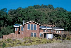 In this solar-powered home, the redwood decking was salvaged from an abandoned sawmill and the existing deck. Salvaged siding, double-pane windows and passive solar heating add to the home's sustainability. Beneath the deck, a 10,000-gallon steel storage tank collects rainwater for irrigation use.